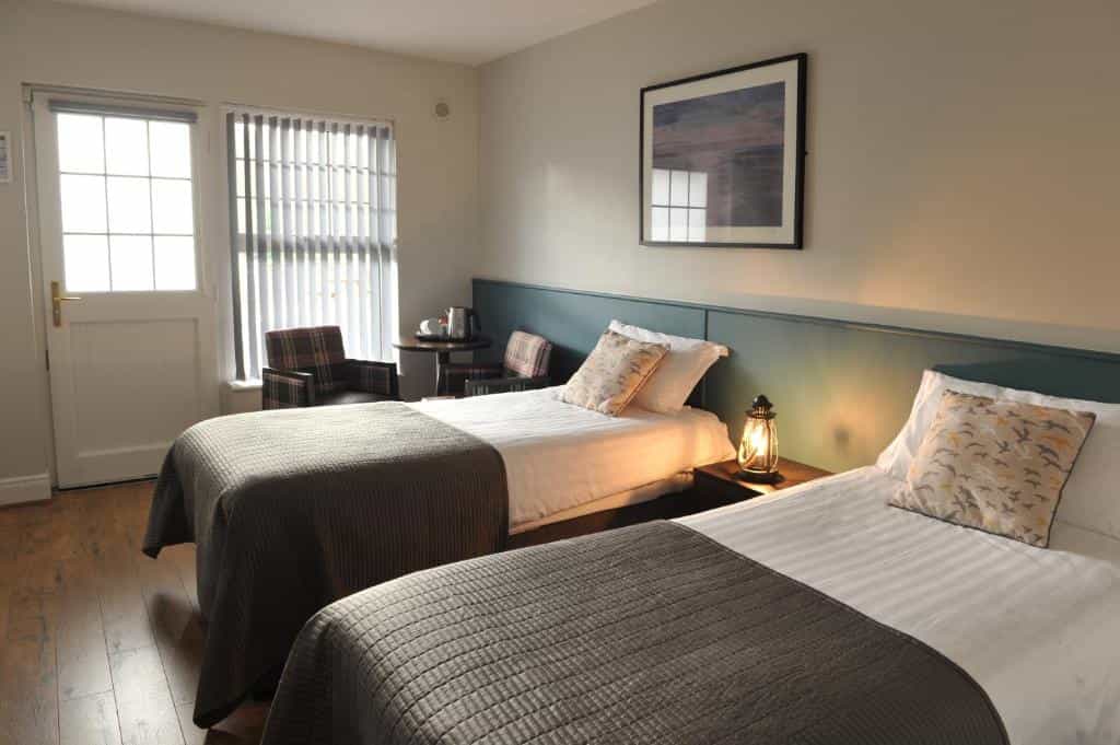 Twin beds in a hotel room with wooden floor, lantern lamp, and view through a door window.