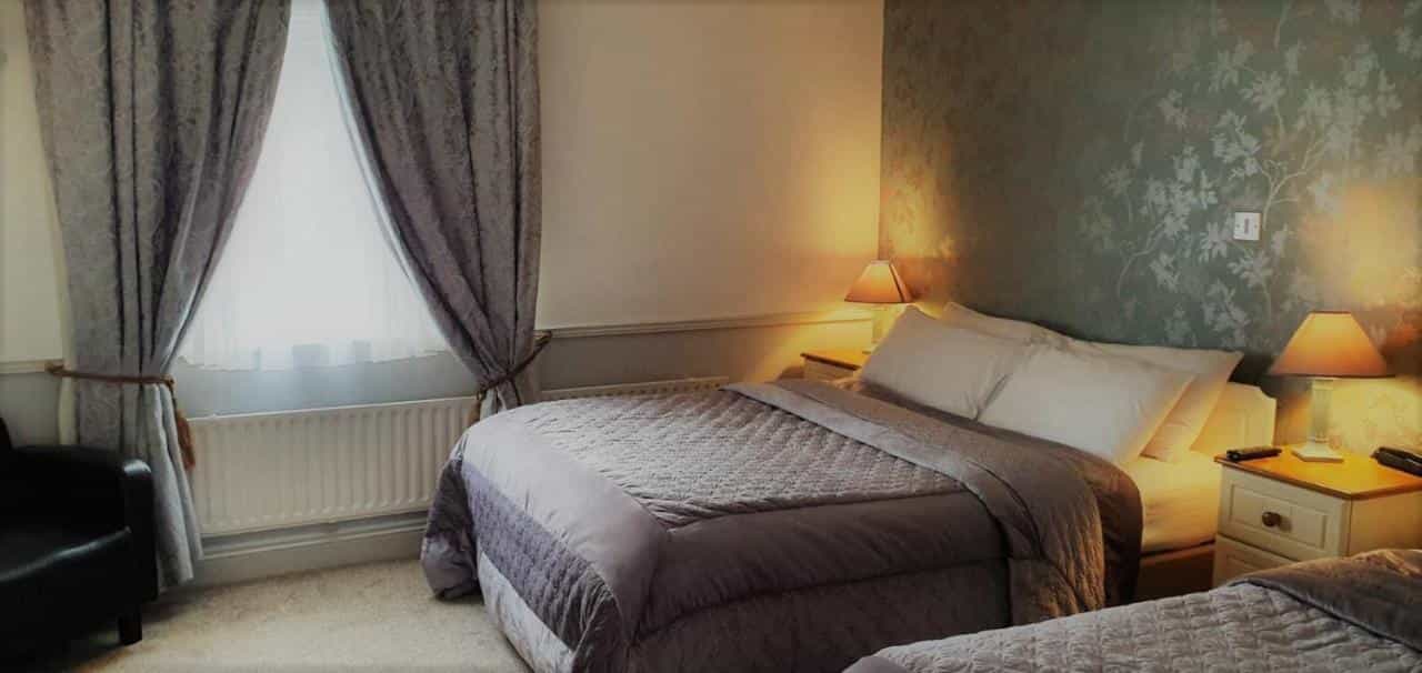 Bedroom in Danagher's Hotel with two beds, patterned wallpaper, and heavy curtains.