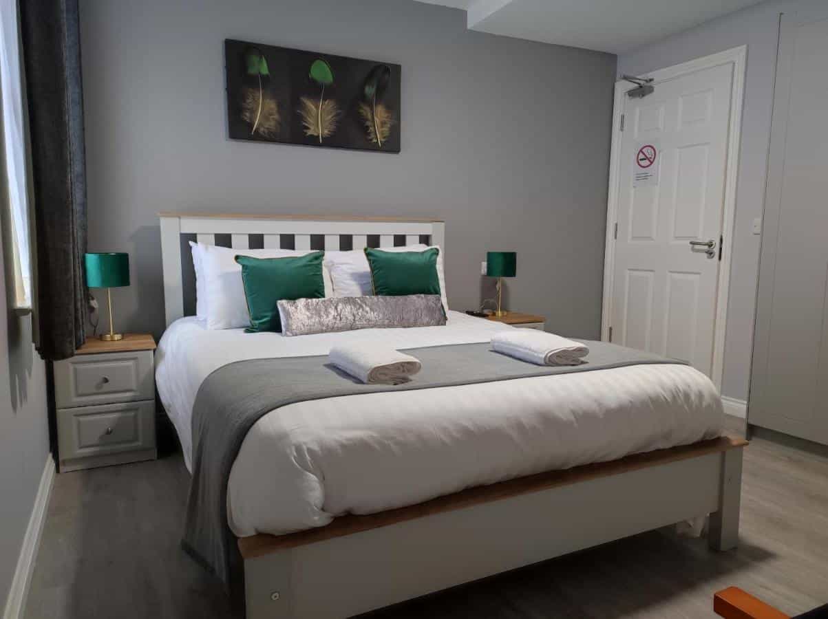 Double bed with white linens, green pillows, and feather art above in a modern room.