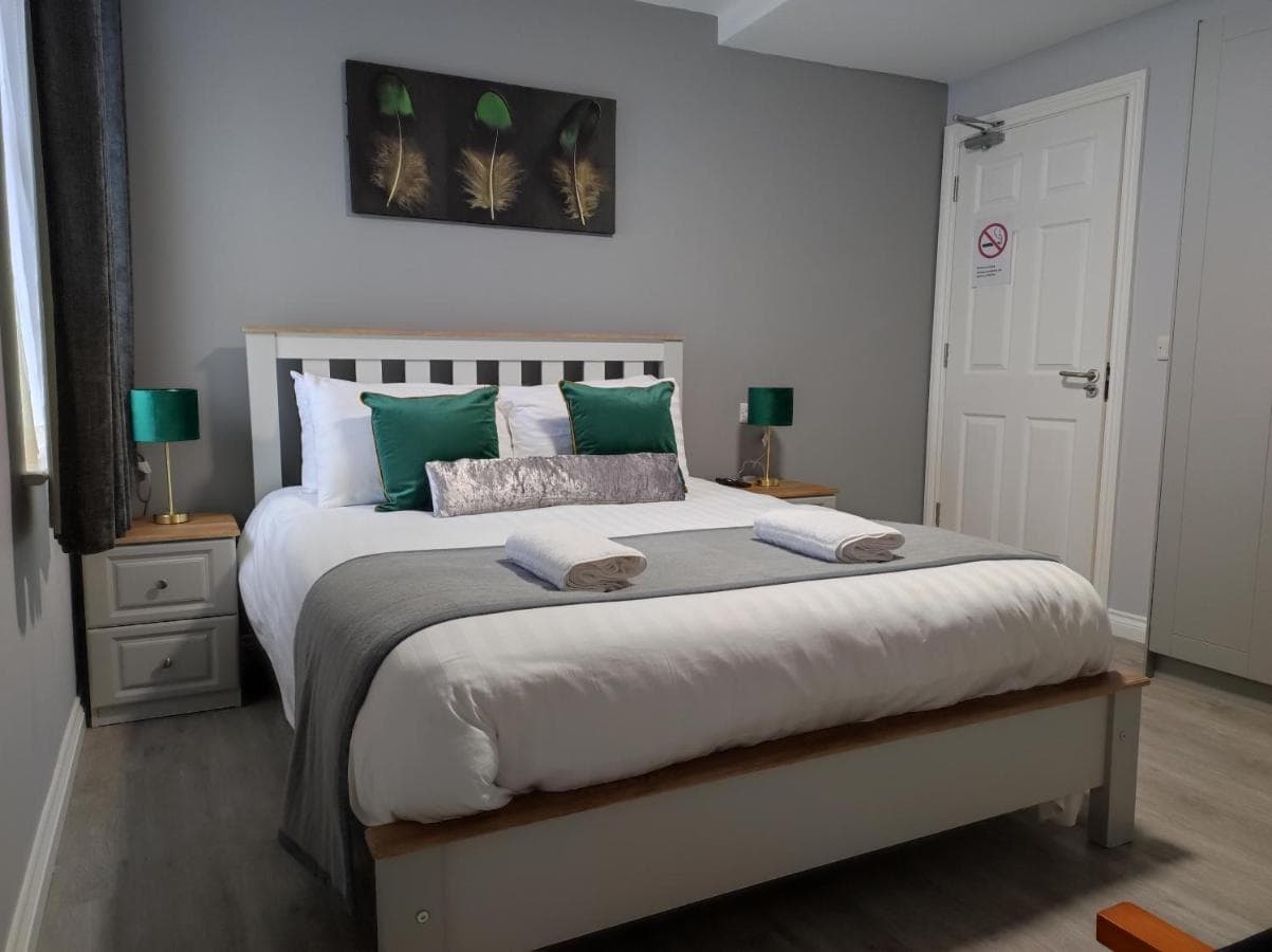 Double bed with white linens, green pillows, and feather art above in a modern room.