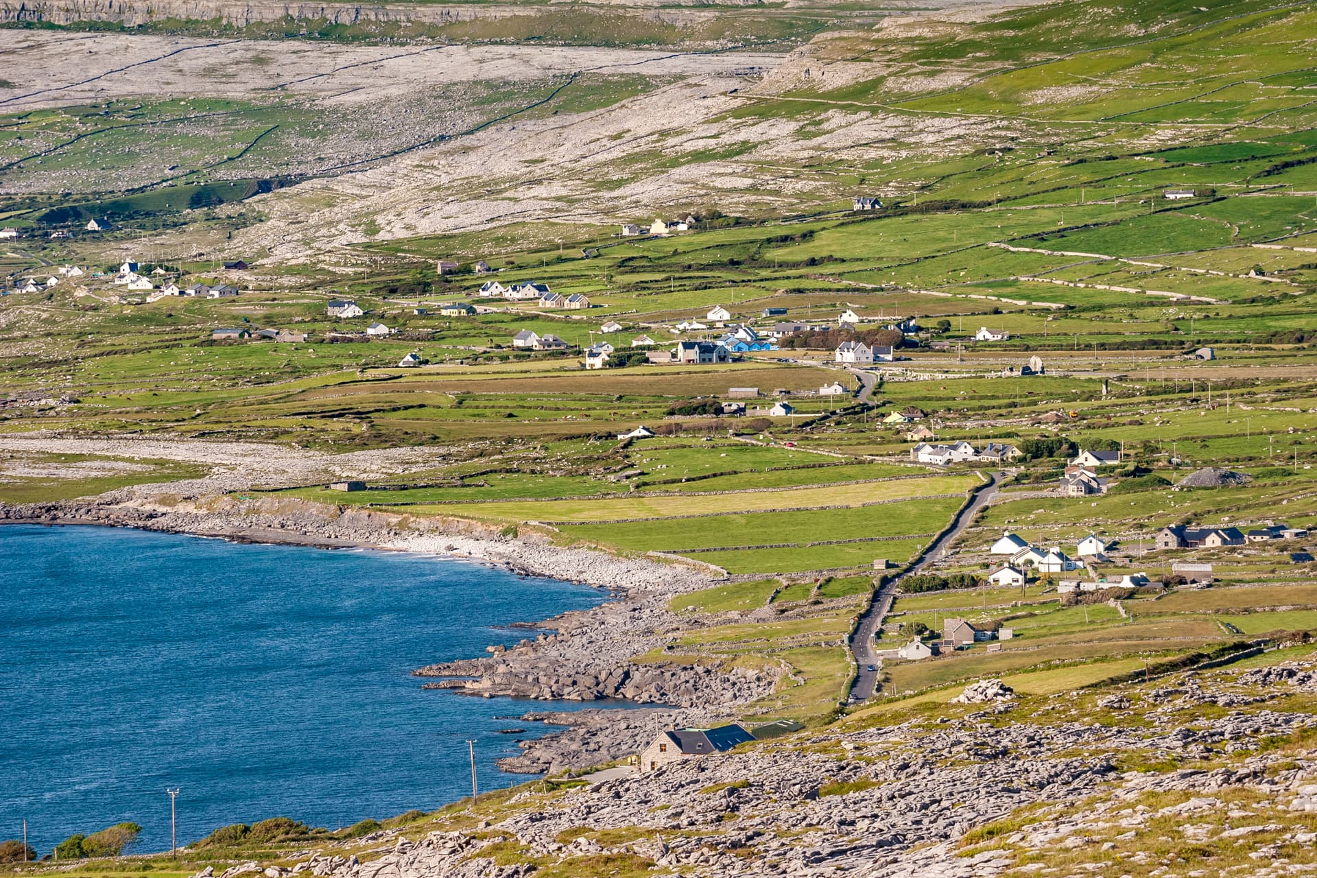 Coastal village nestled among green fields and rocky terrain above blue sea in Ballyvaughan.