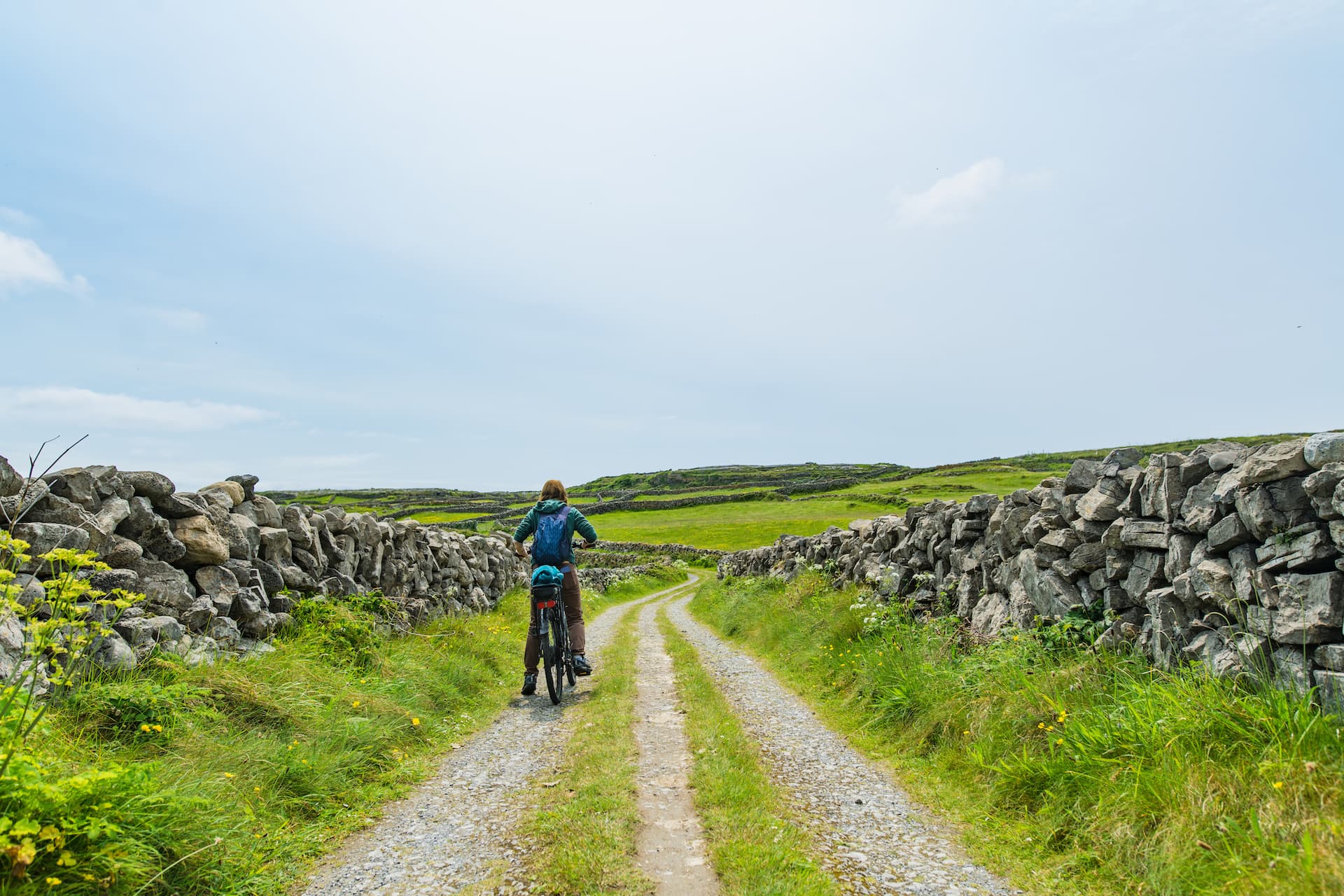 Cyclist on gravel path between stone walls in green rolling landscape