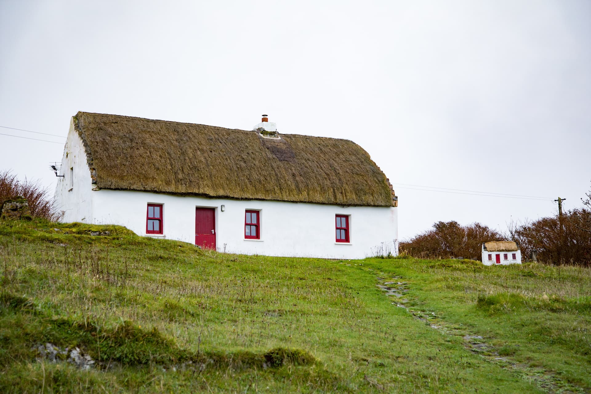 White thatched cottage with red trim on grassy hillside in Inishmore