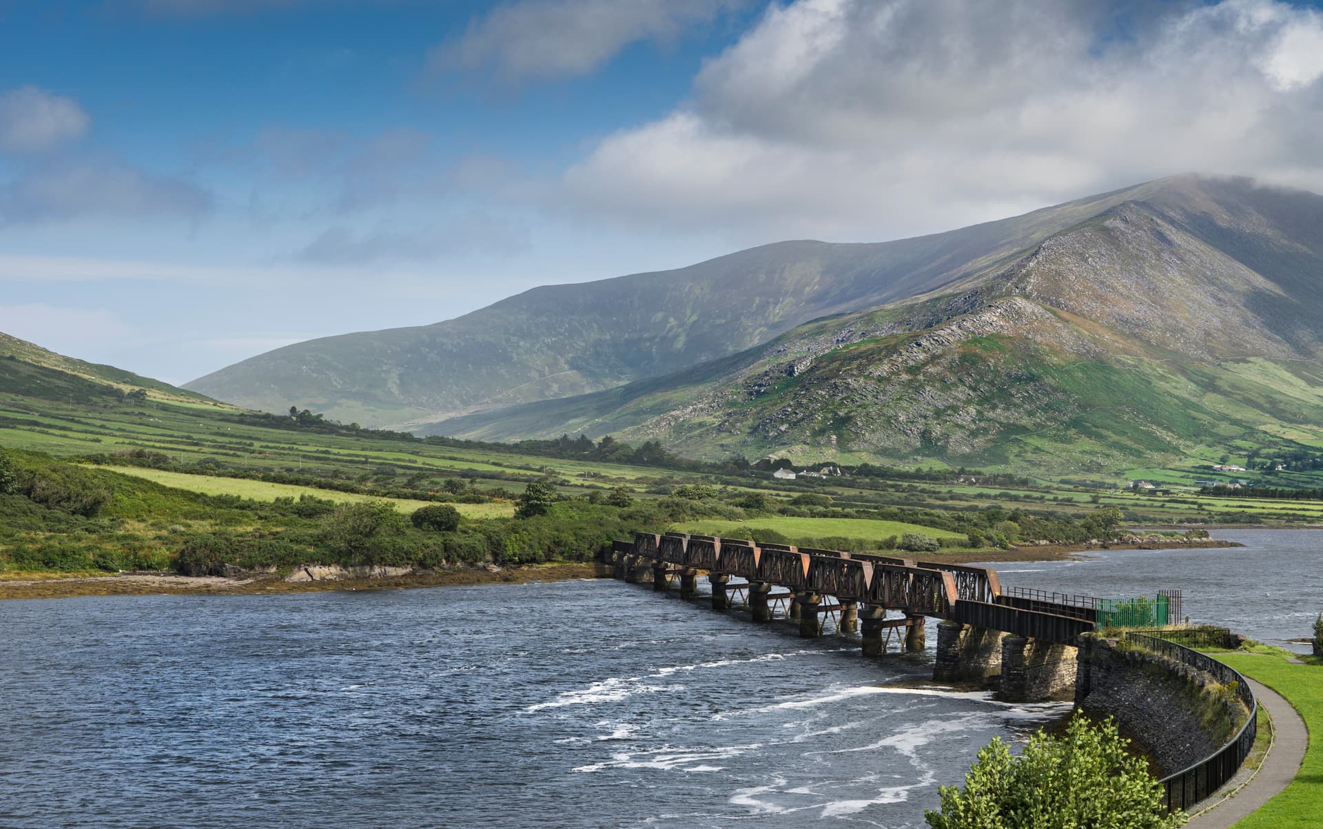 Old railway bridge over water with green hills and mountains in Cahersiveen.