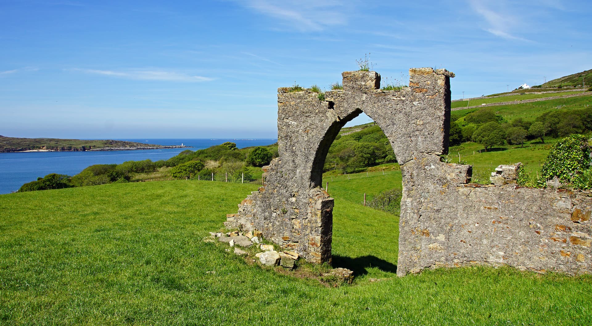 Stone ruin archway overlooking green hills and the sea near Clifden Castle.