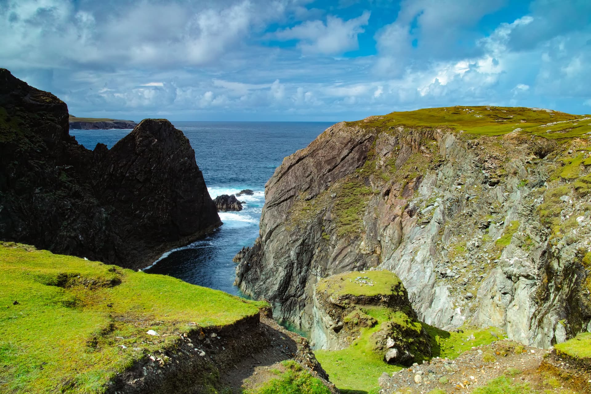 Cliffs overlooking the sea with green grassy tops and dramatic blue sky at Inishbofin.