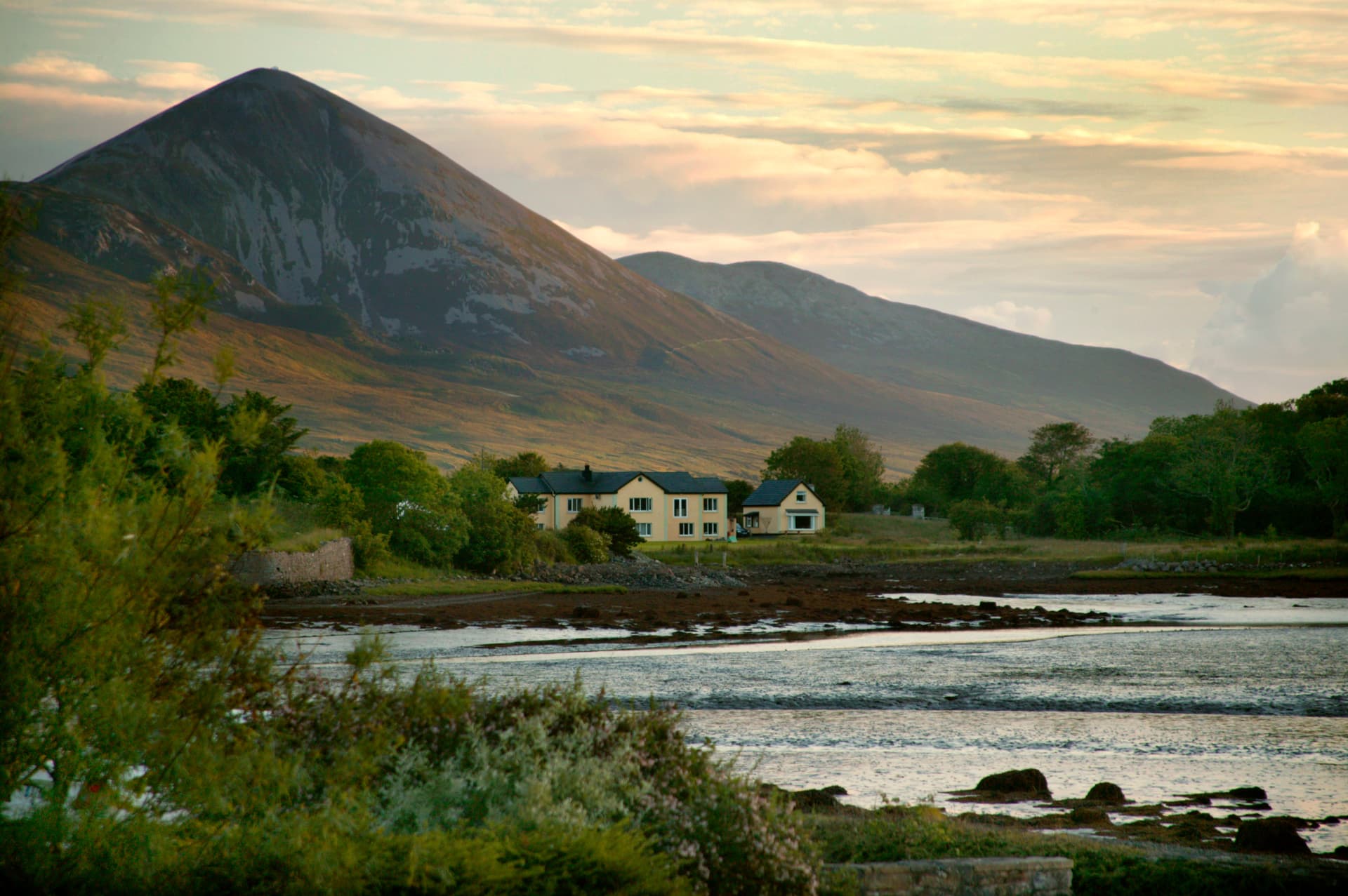House nestled at the base of Mt. Croagh Patrick overlooking tidal flats at sunset.