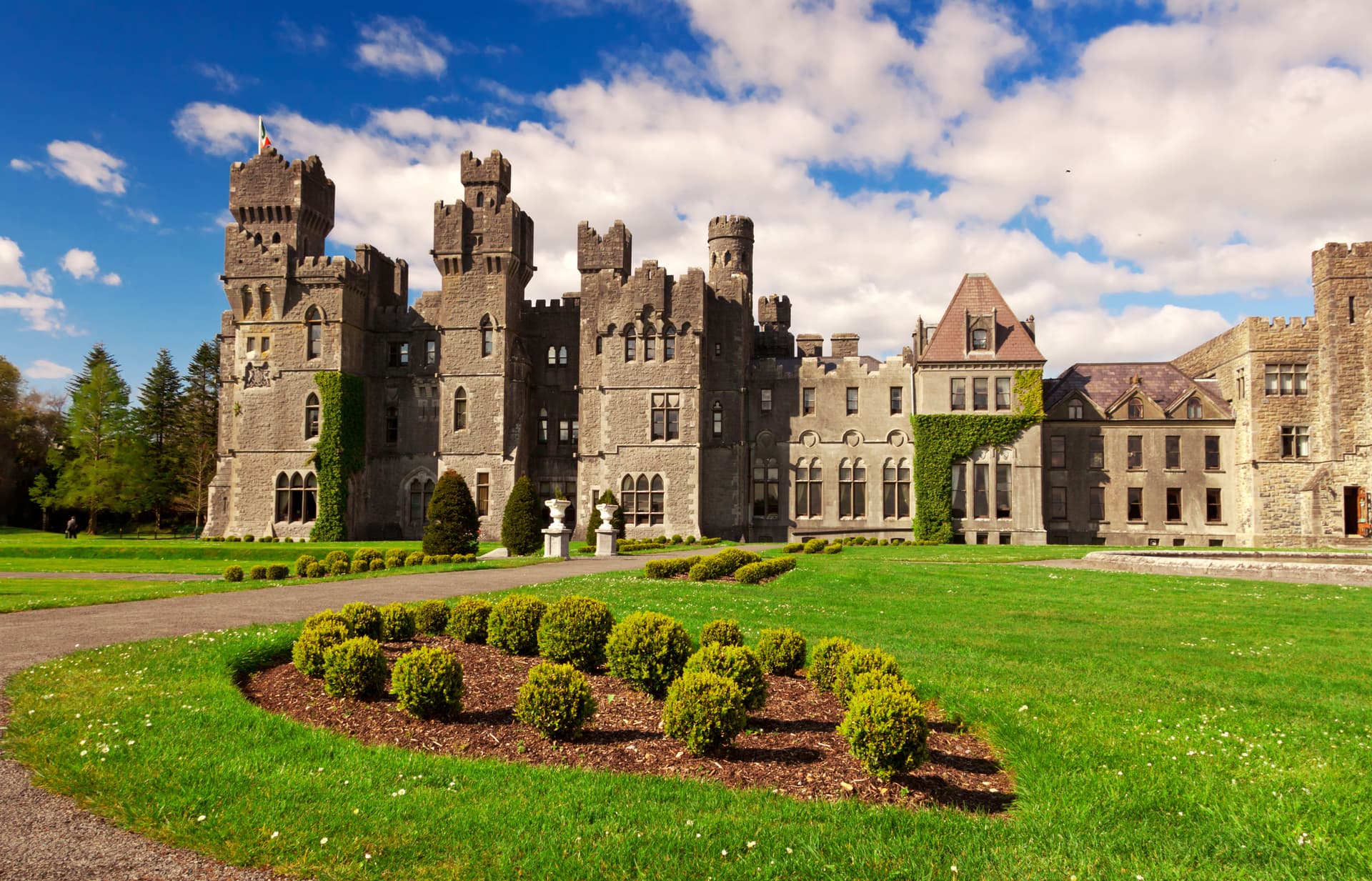 Ashford Castle near Cong with stone towers, green lawn, and bright blue sky.