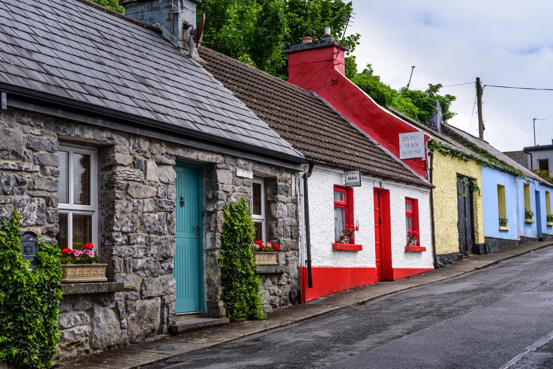Colorful stone cottages with slate roofs lining a wet, uphill street.