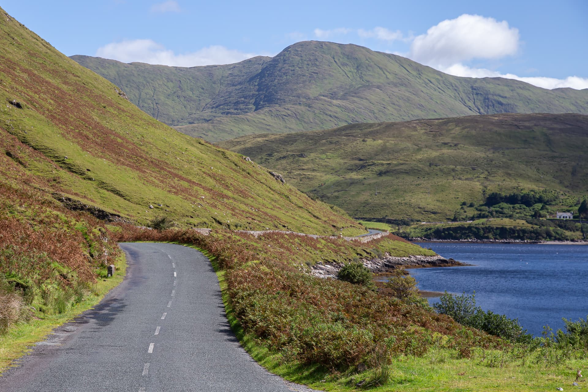 Paved road winding alongside green hills and blue water, Killary Harbour visible