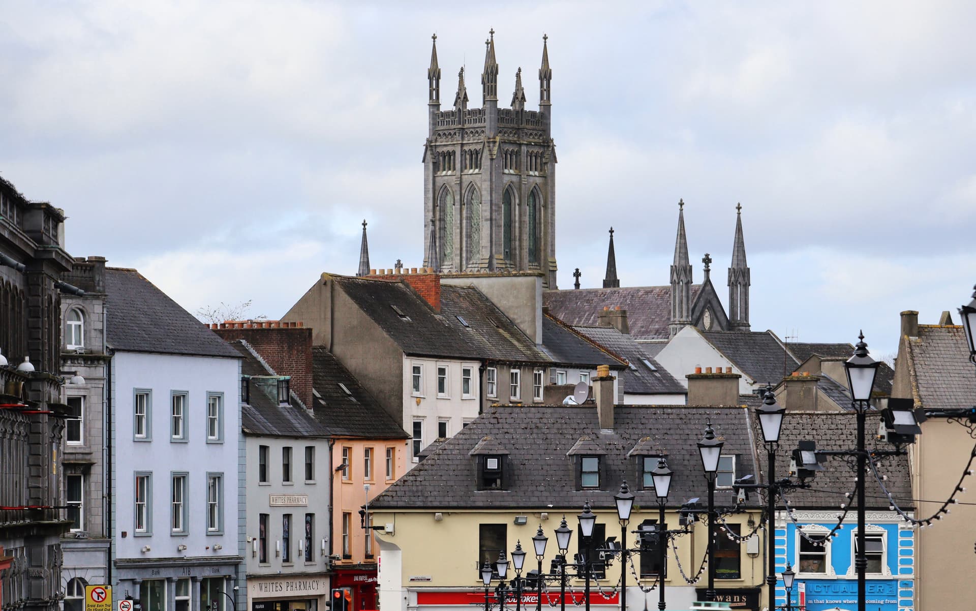 Gothic cathedral spire rising above colorful buildings and street lamps in Killarney.