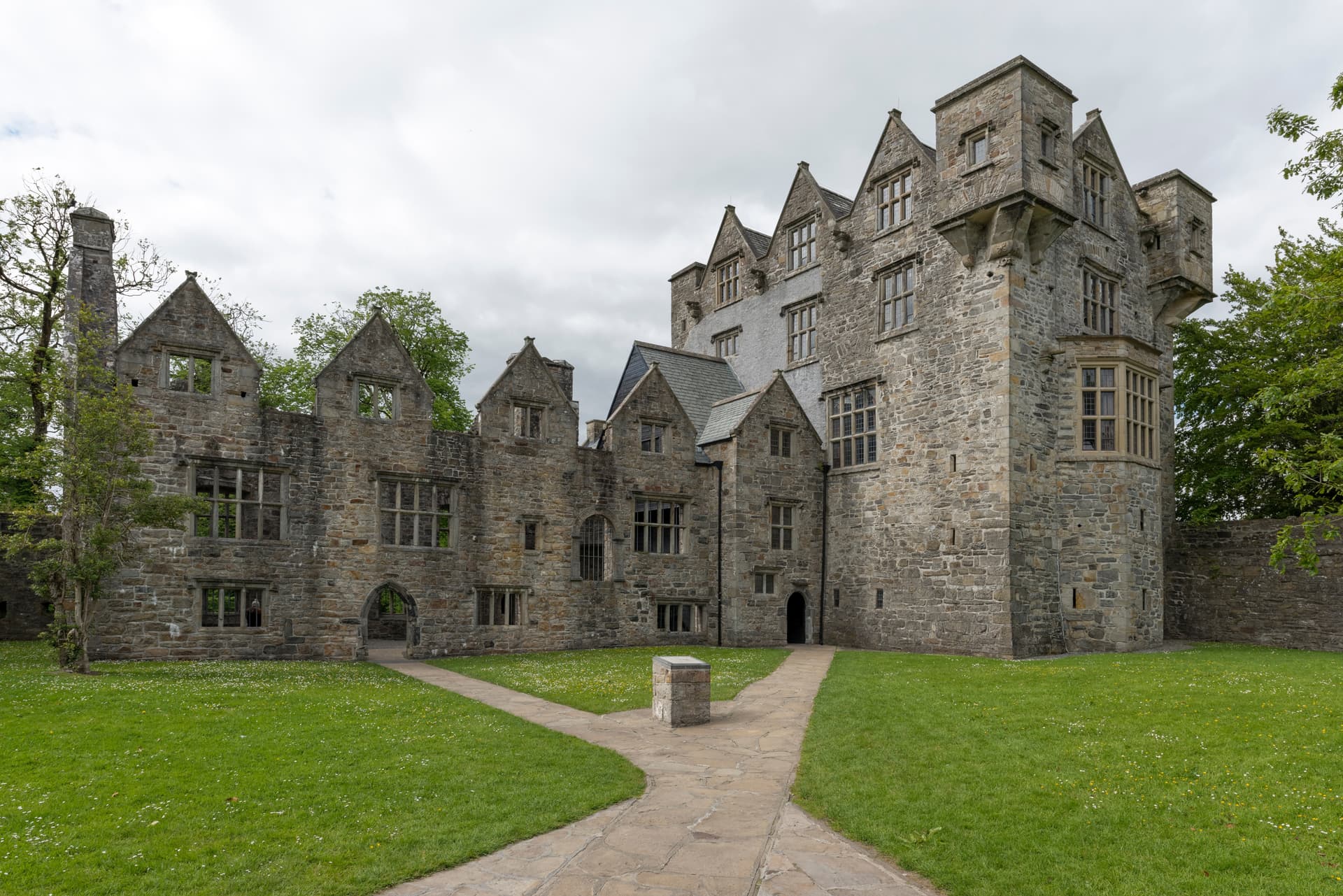 Stone ruins of Donegal Castle with green lawn and flagstone path under an overcast sky.