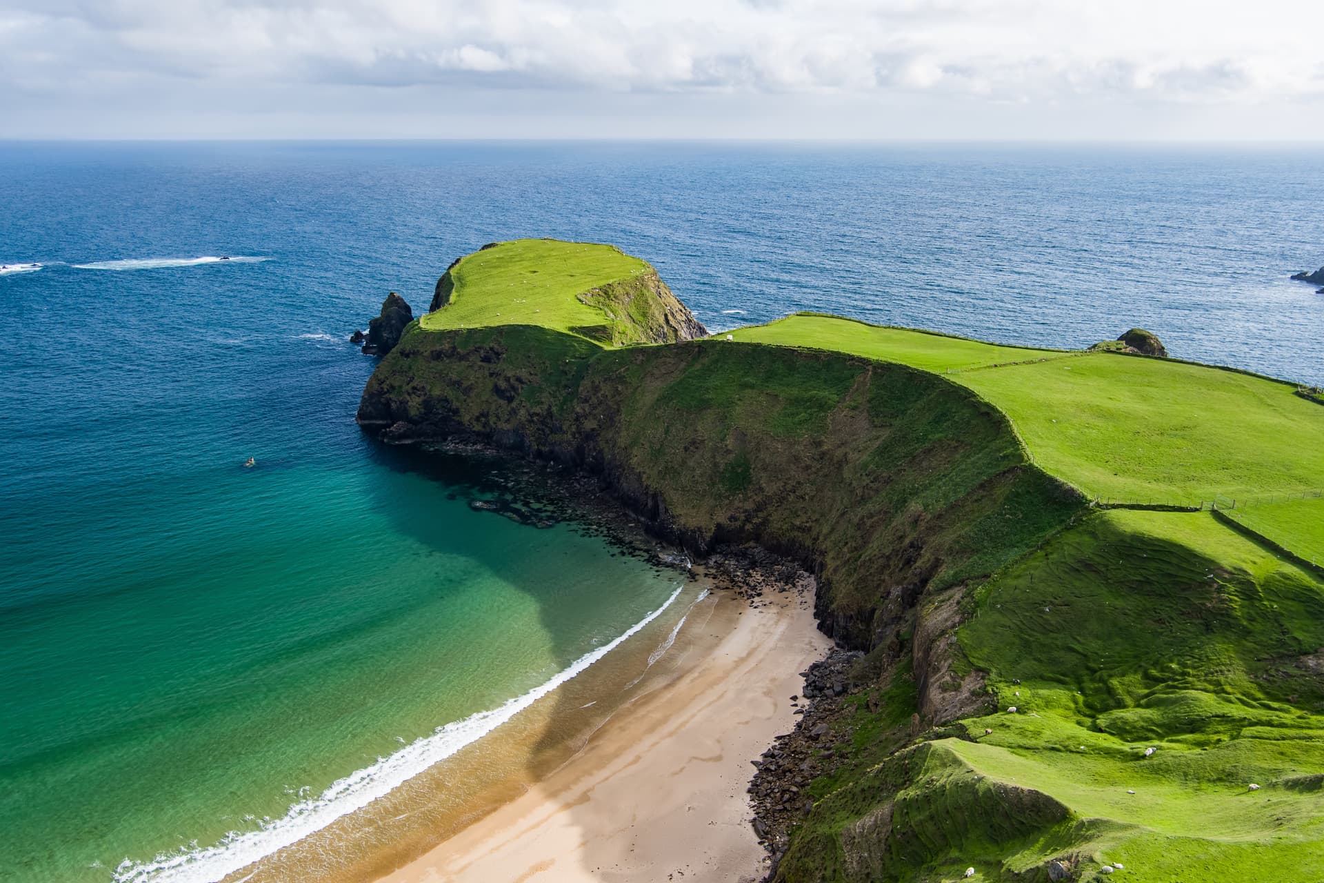 Green cliffs near Glencolmcille overlooking turquoise water and a sandy beach.