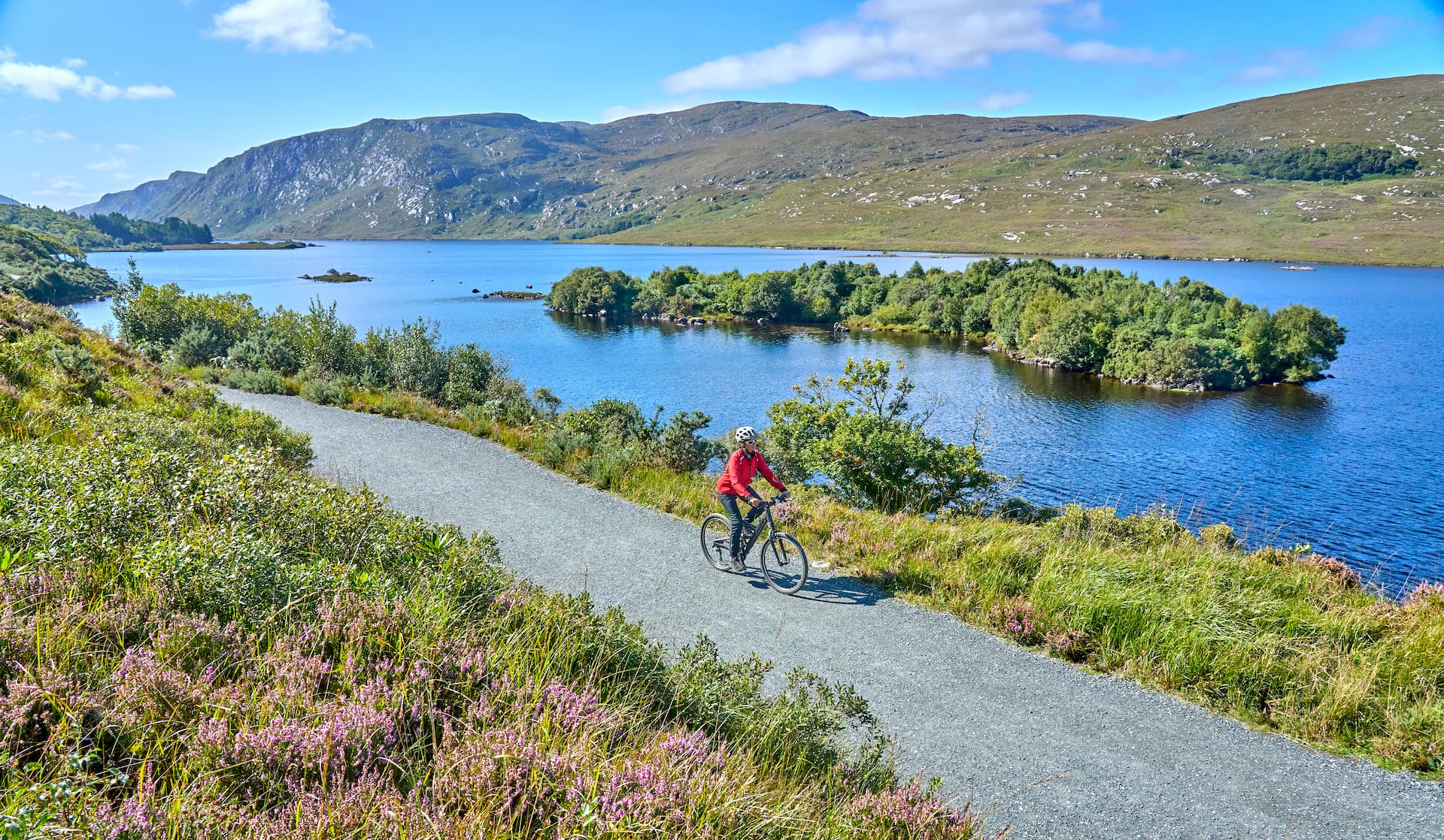 Cyclist on gravel path beside lake with mountains in Glenveagh National Park