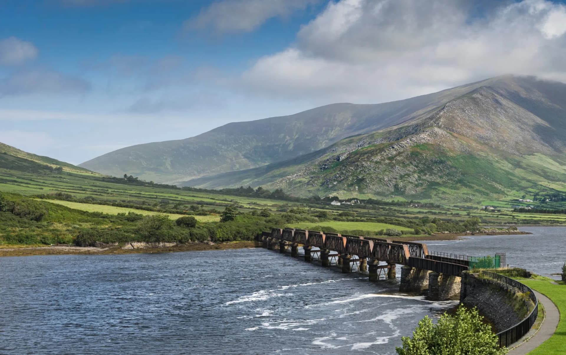 Railway bridge crossing water with green hills and mountains in Cahersiveen, Ireland.