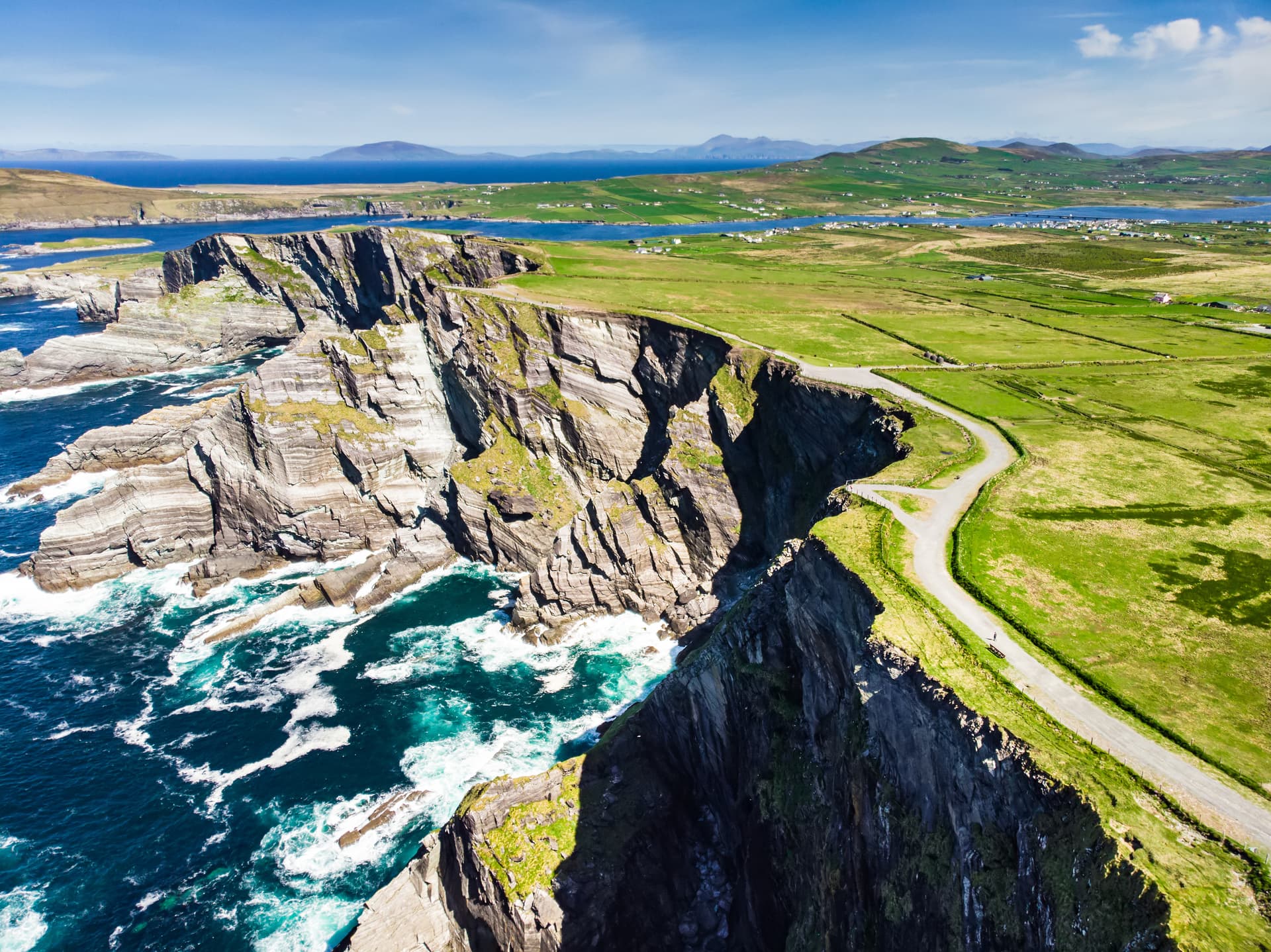 Dramatic sea cliffs with a walking path on green coastal land overlooking the Atlantic Ocean.