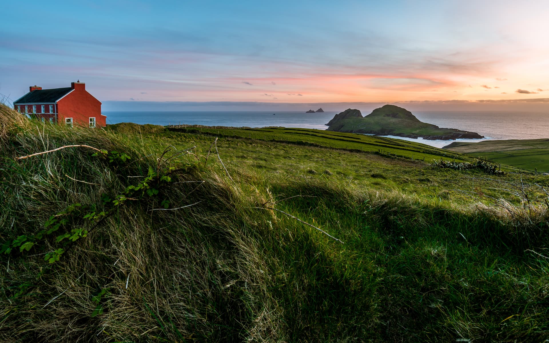 Red house on grassy hillside overlooking Skellig Islands at sunset