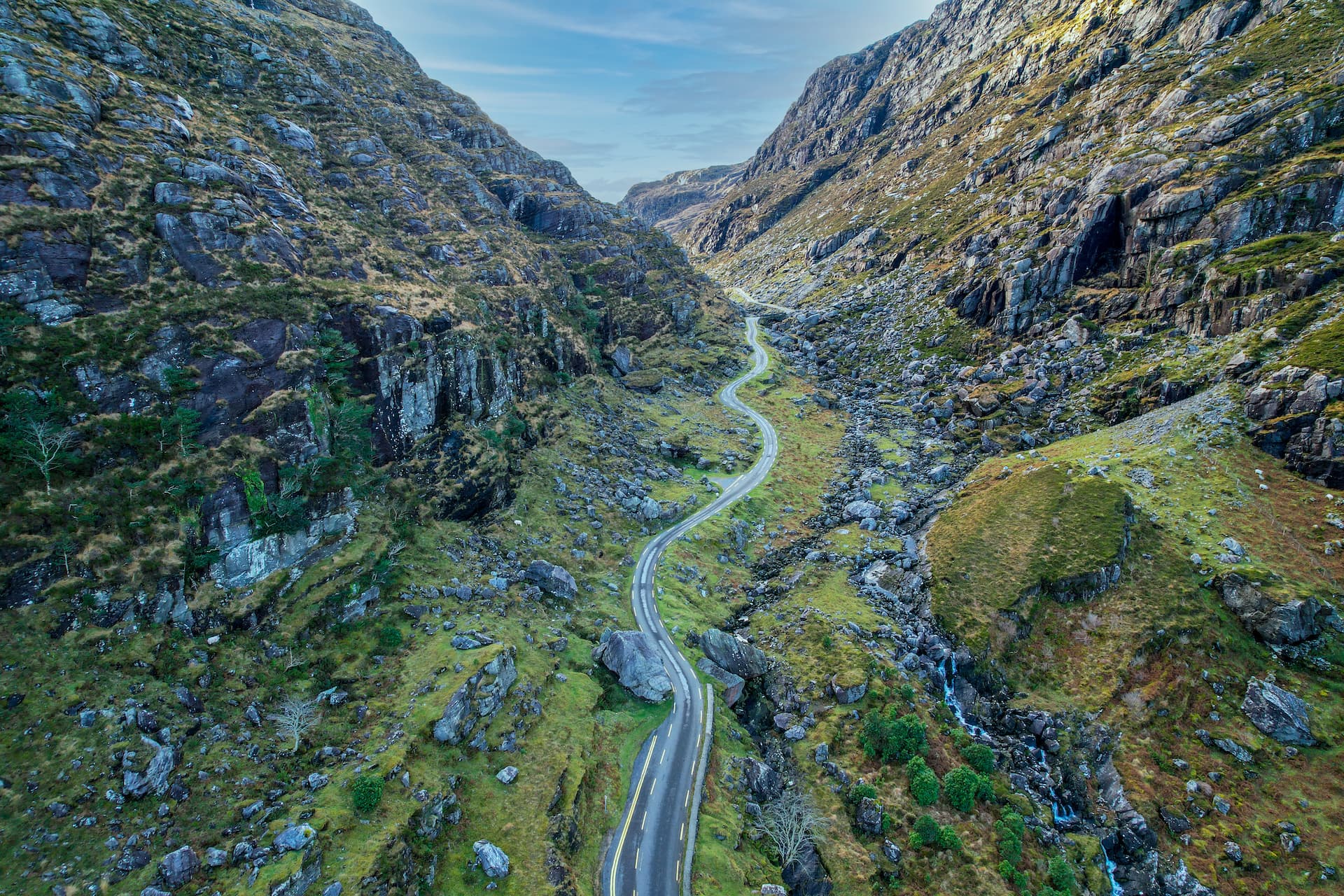 Winding road through the Gap of Dunloe valley with steep, rocky, green mountainsides.