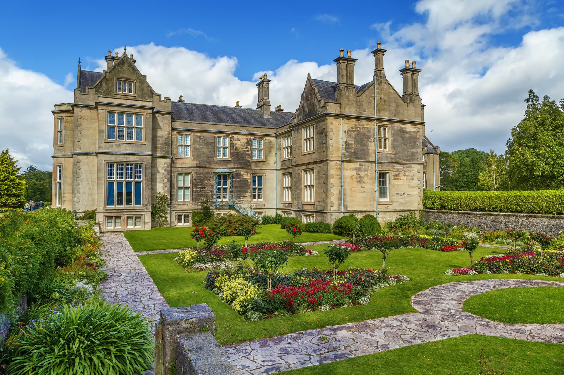 Muckross House in Killarney with formal gardens, stone paths, and blue sky.
