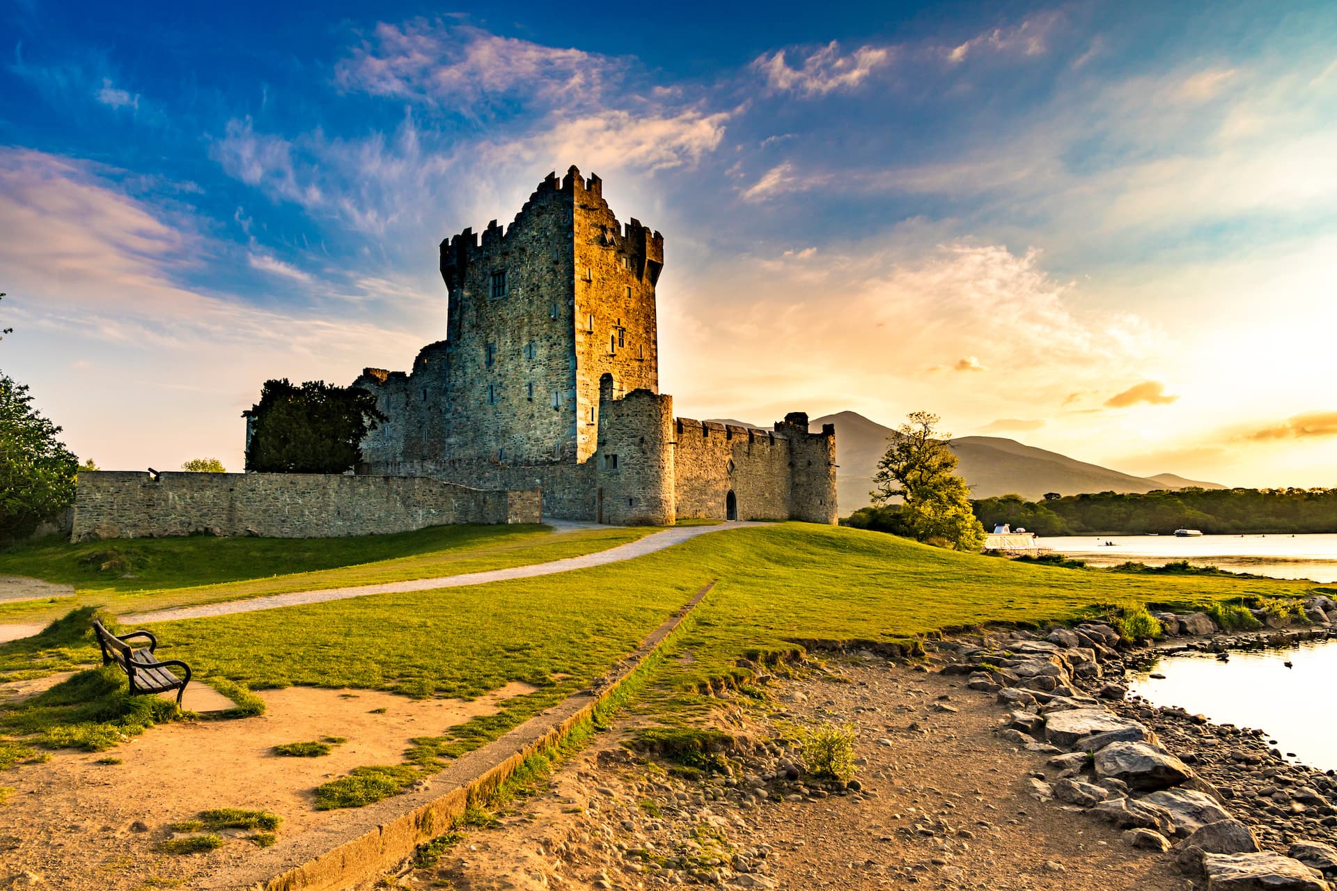 Ross Castle Killarney on grassy hill by lake at sunset with mountains in background