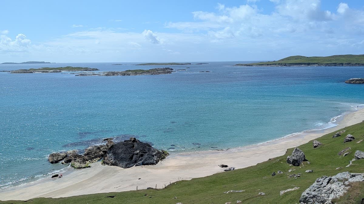 Sandy beach with rocky outcrops and turquoise coastal waters under a blue sky with clouds