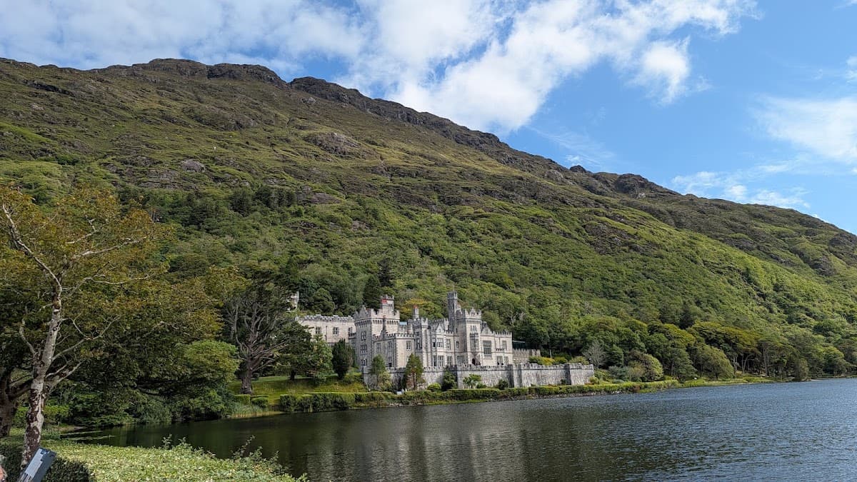 Historic stone castle nestled on a lakeside shore beneath a steep, forested mountain.